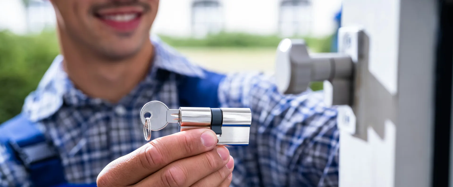 Smiling locksmith holding a new silver door cylinder lock and key, ready for installation.