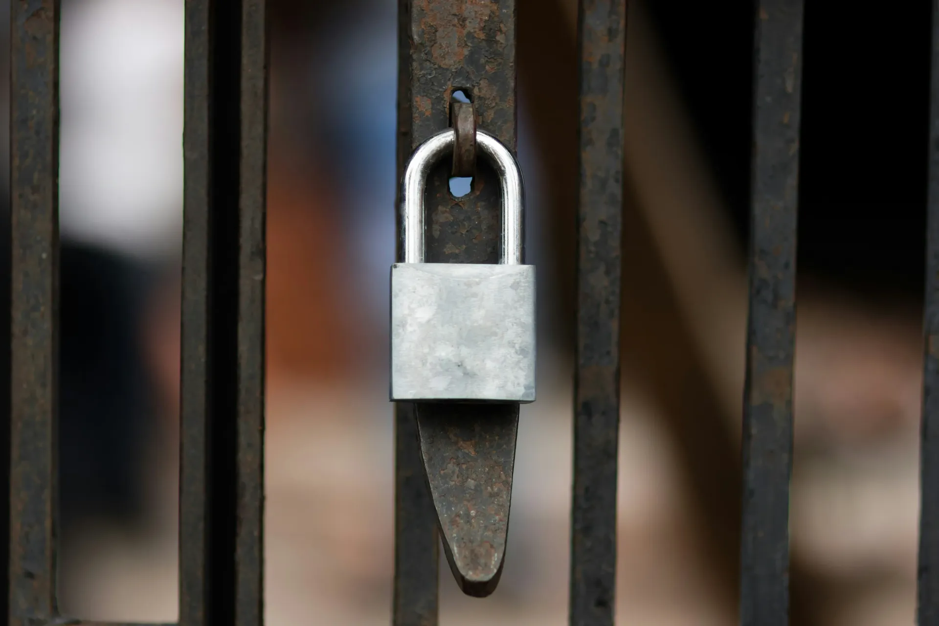 A shiny silver padlock fastened onto dark, rusty metal bars or a gate.