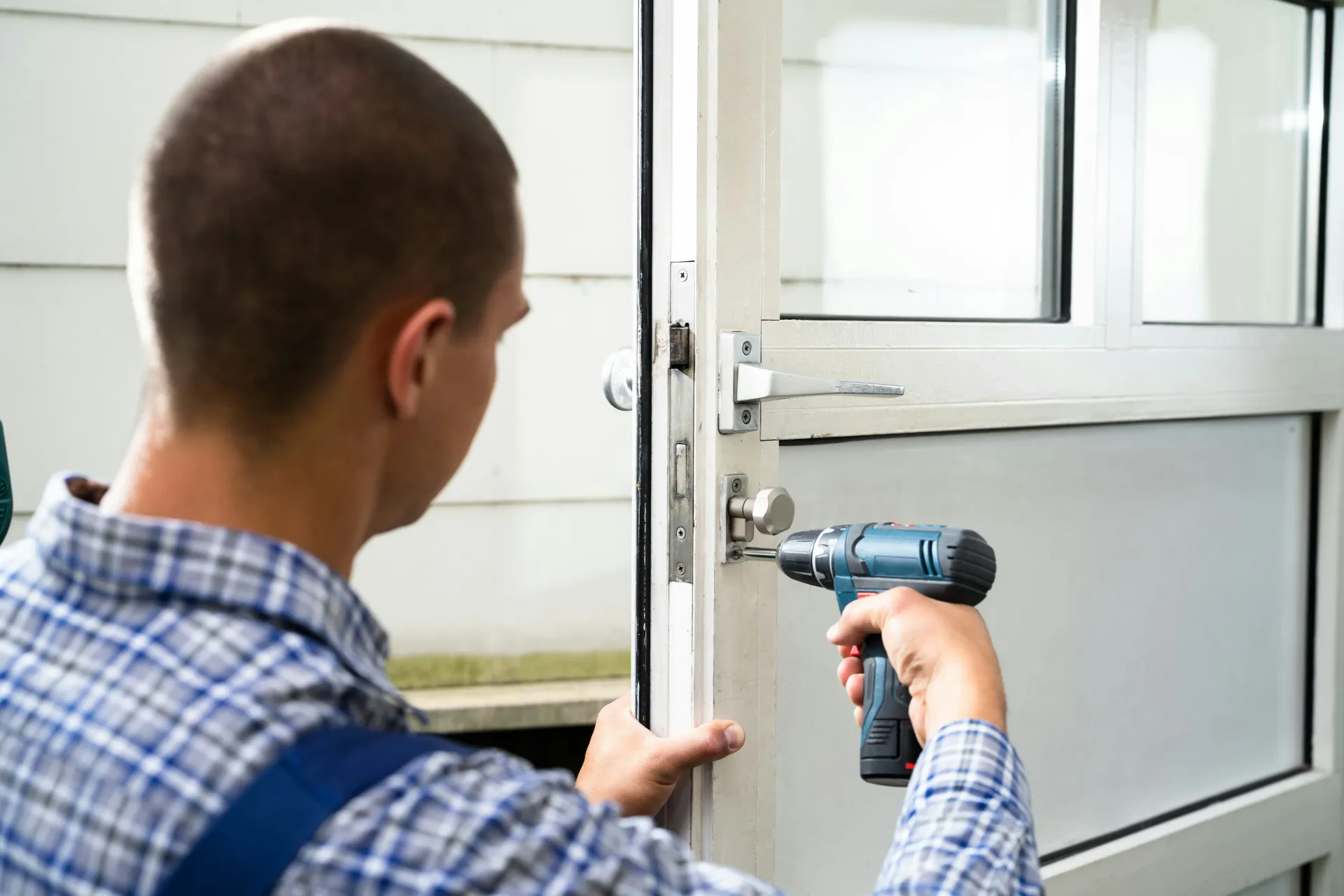 A close-up of a locksmith using a cordless drill to repair or install a lock on a white uPVC door.